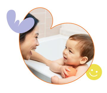 Mom is smiling at her baby boy who is holding an orange bath toy ball