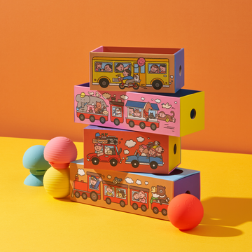 Stack of b is for ball® and colorful toy boxes with whisical illustrations on an orange and yellow background