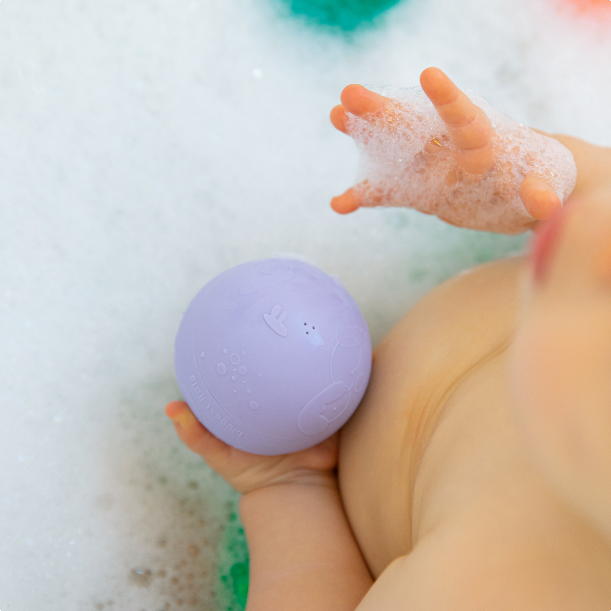 Baby holding a purple bath toy ball from B is for Ball
