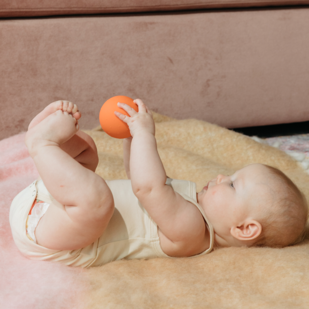 6-month-old baby holding B is for Ball toy for sensory play