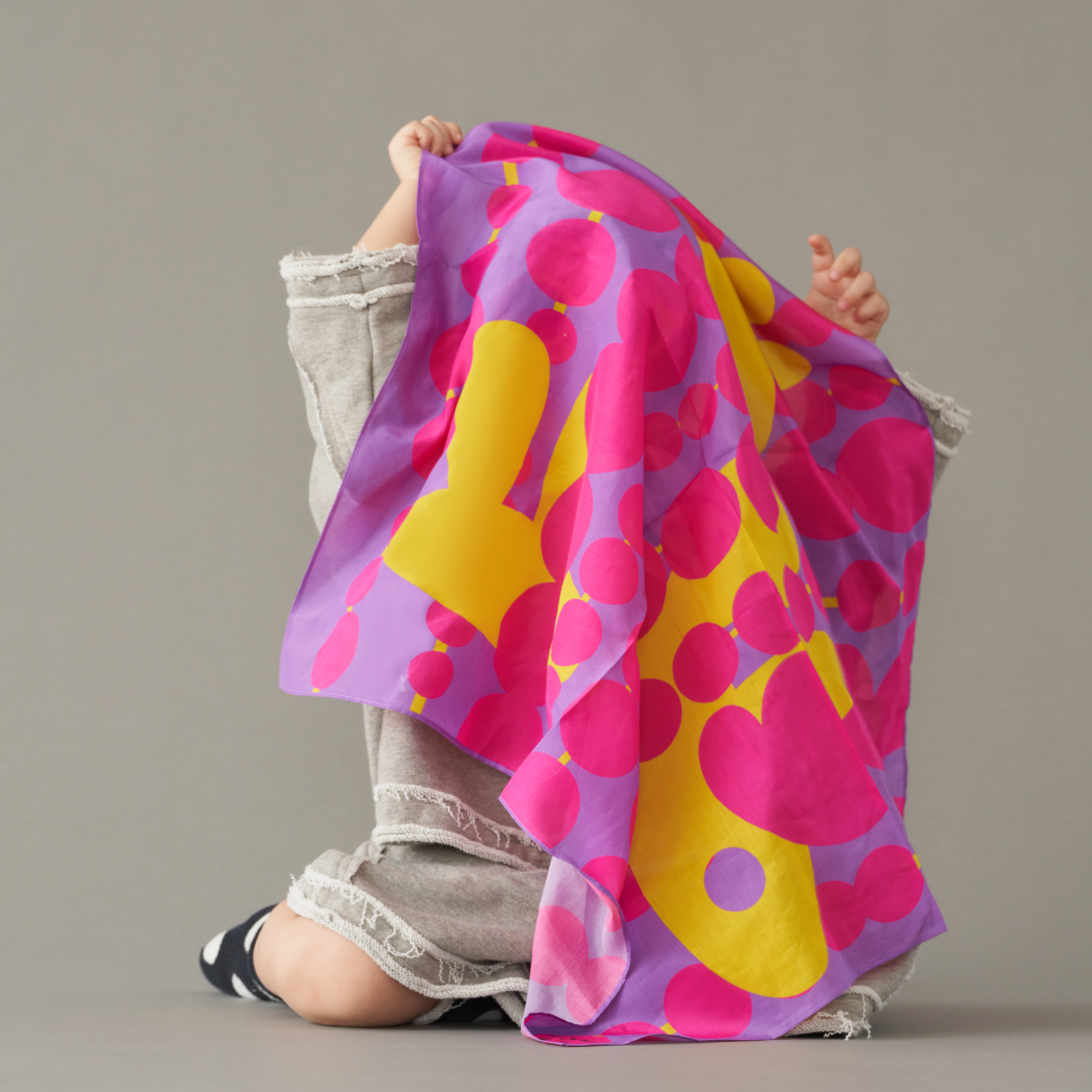 Toddler holding a art play silk in hide and seek print - purple polkadots with yellow abstract design - on a plain background