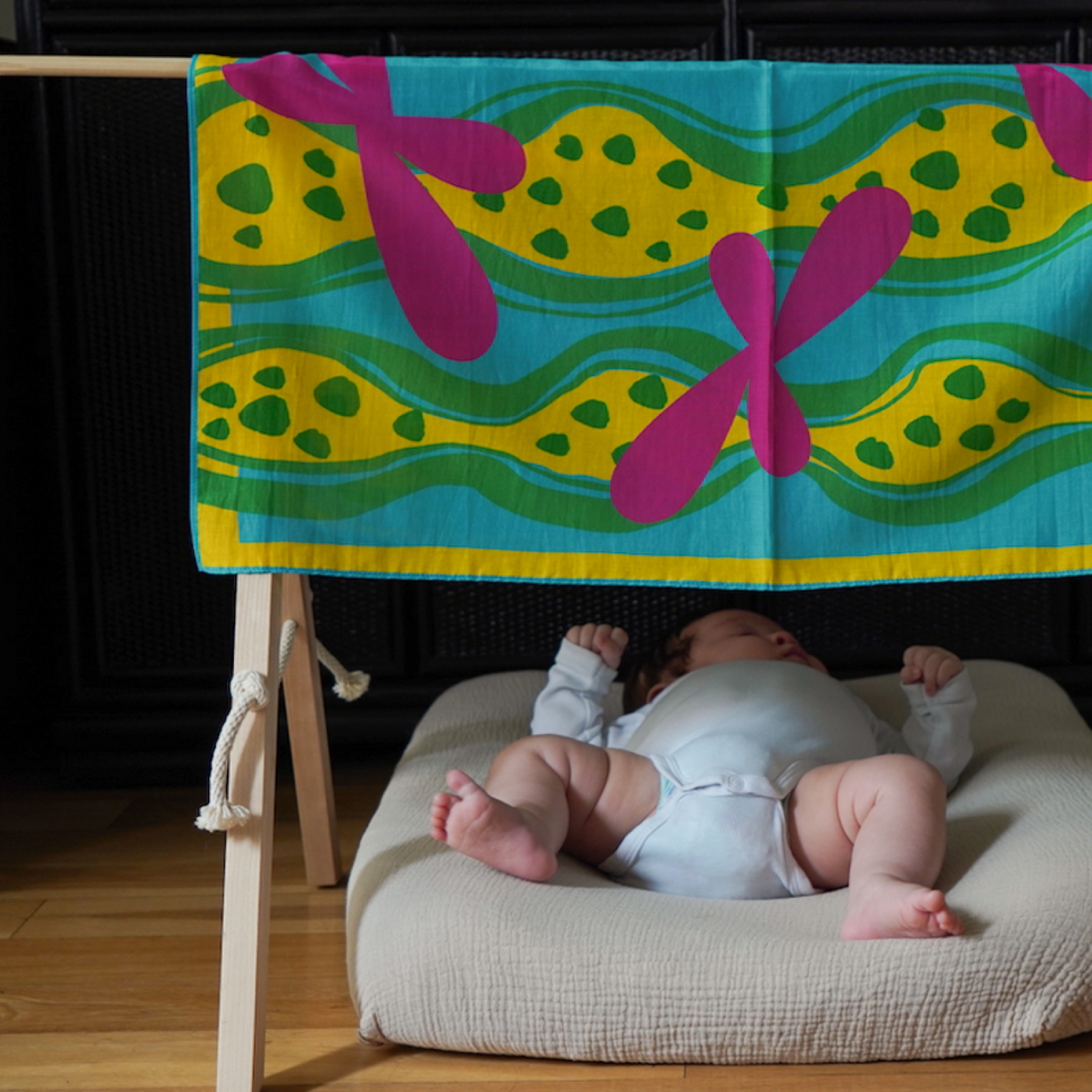 Baby lying on a cushion under a colorful art play silk canopy in dots and friends print