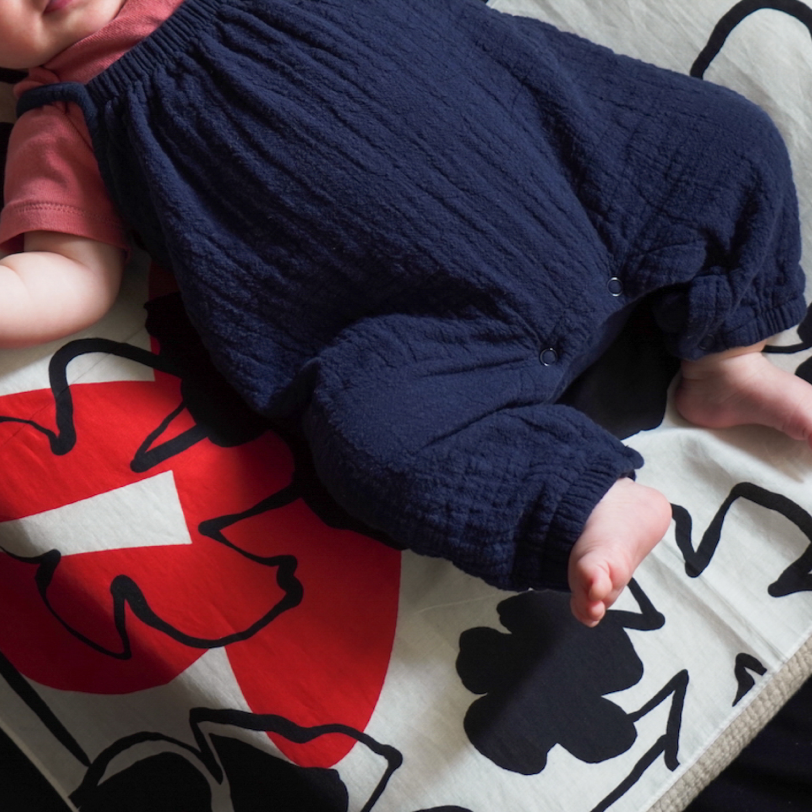 Baby wearing navy blue onsies lying on art play silk in secret garden print