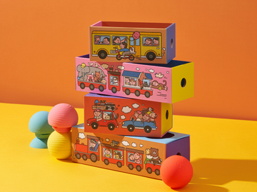 Stack of b is for ball® and colorful toy boxes with whisical illustrations on an orange and yellow background