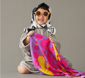 A toddler wearing sunglasses and holding a art play silk with bright smile