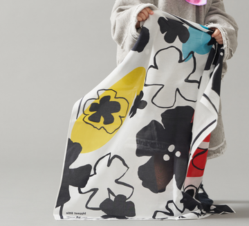 A toddler holding a art play silk in secret garden print which naturally drapes on the ground