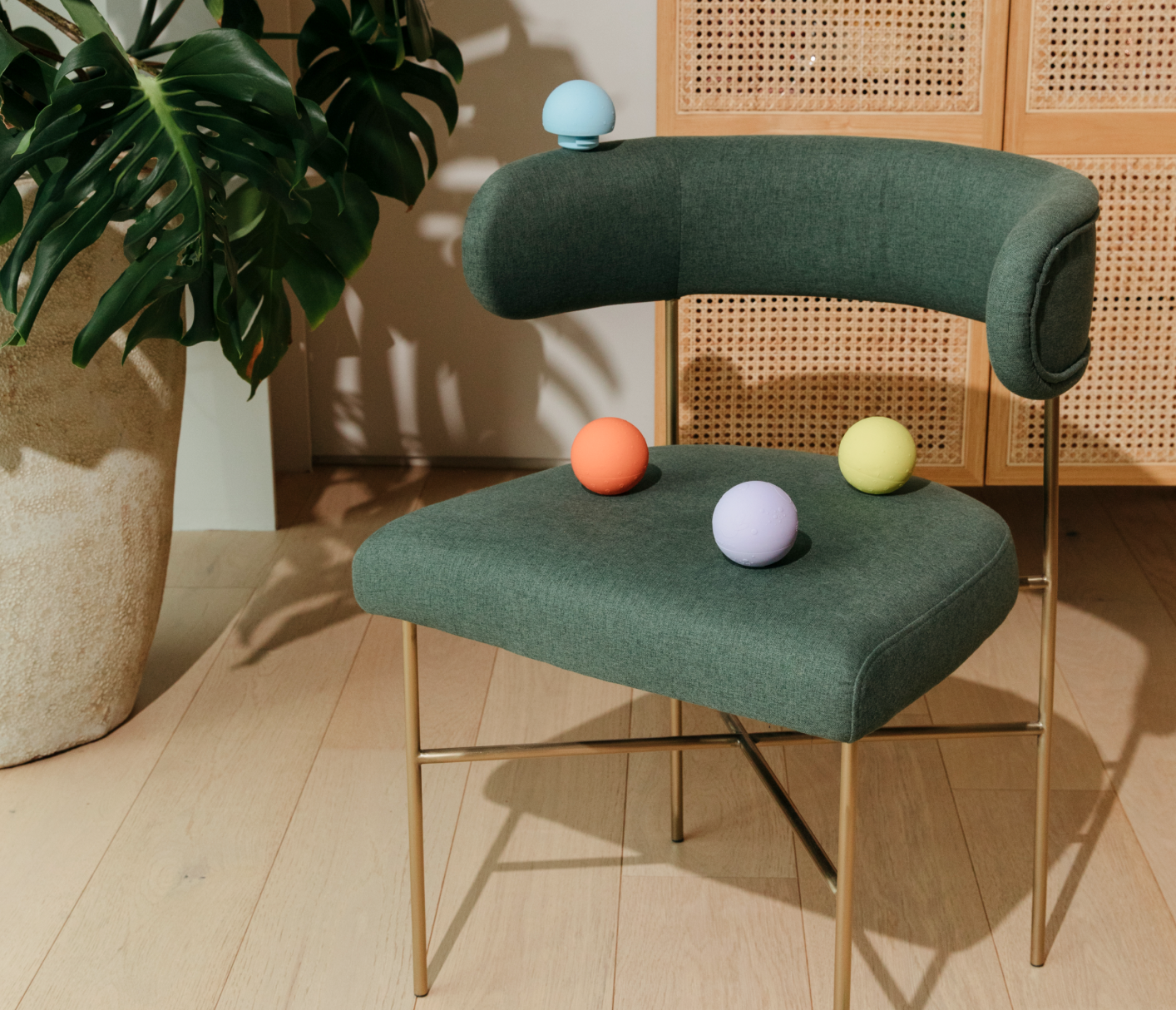 blue, orange, purple and yellow toy balls are displayed on a mid-modern century green chair with gold accent legs 