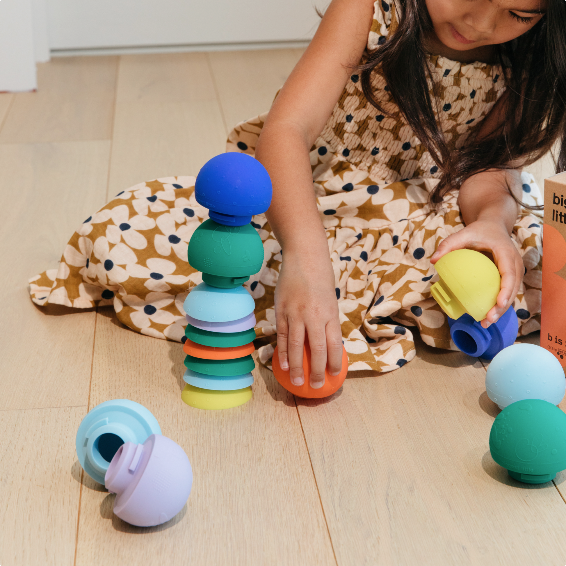 A toddler girl is stacking bright colored lids and bodies of the detachable ball toy b is for ball™